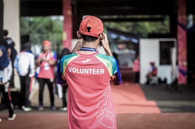 Back of man in red "Volunteer" shirt who is taking a photo of other volunteers